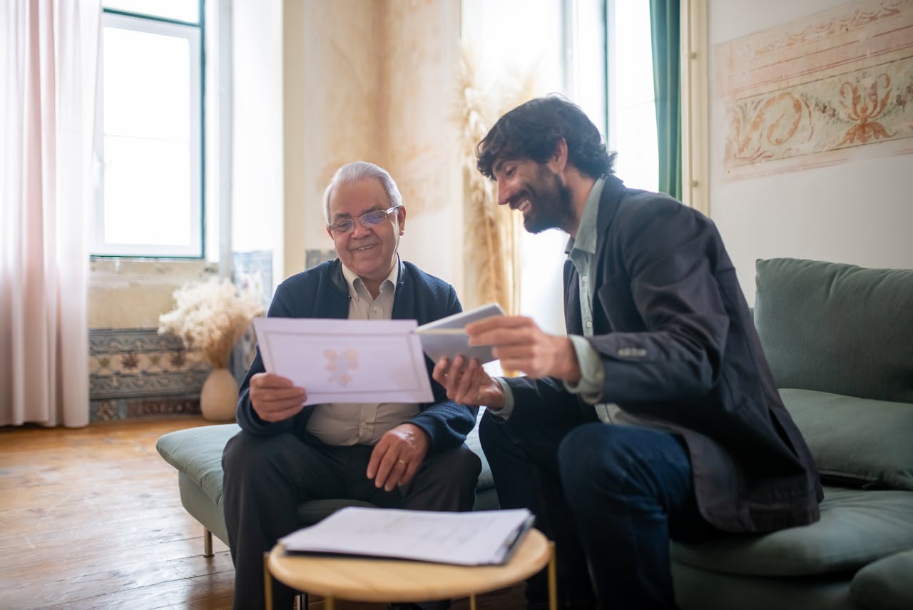 Two men seated on a couch, examining papers together with focused expressions.