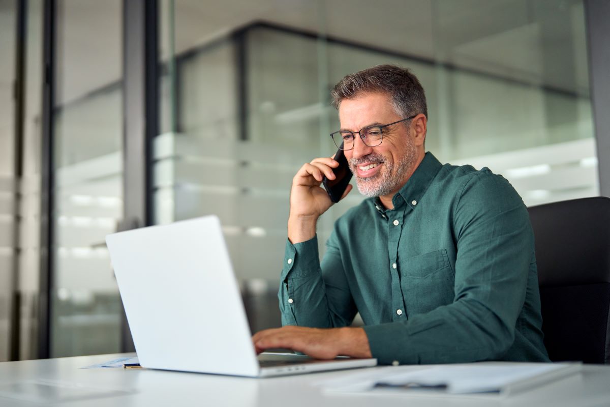 Man talking on a phone sitting in front of his laptop