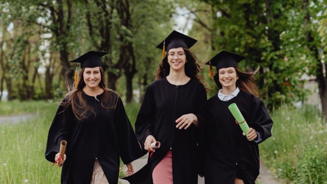 Three female graduates in gowns walking together along a path