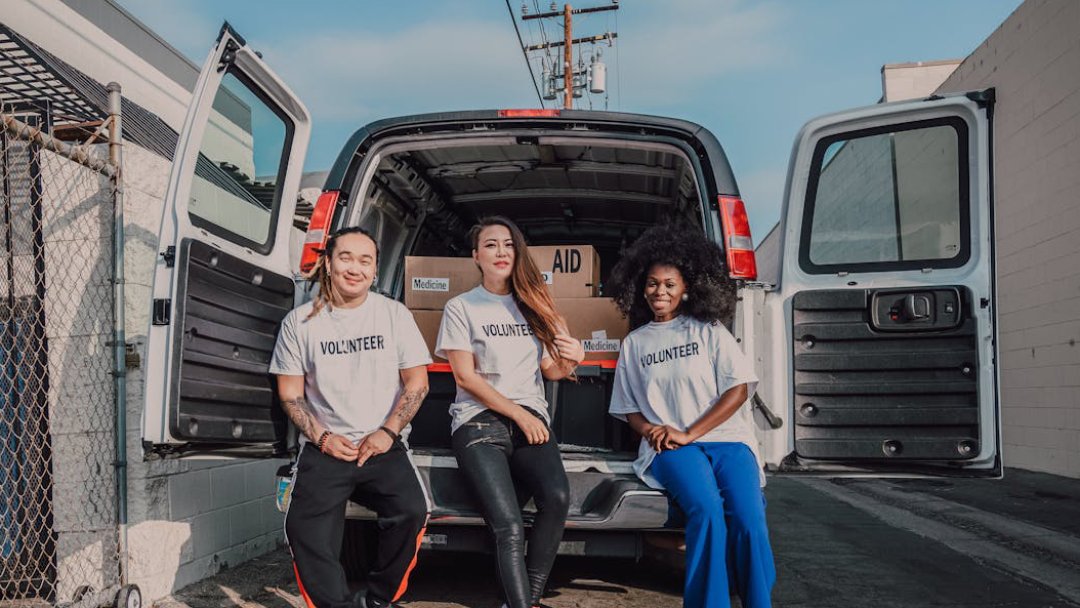 Three women in white shirts stand together in front of a van